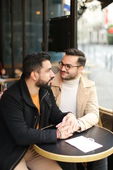 Two american handsome gays talking at street cafe and holding hands. Concept of same sex couple and lgbt.