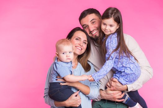 Cute family posing and smiling at camera together on pink background.