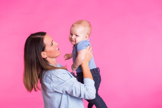 Loving mother playing with her baby boy on pink background.