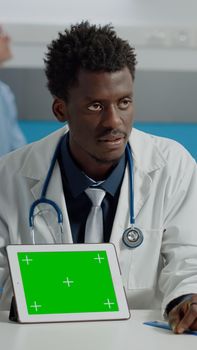 Man working as doctor pointing at green screen on modern tablet in office. Medic with horizontal mockup template and isolated chroma key technology for appointment at medical facility
