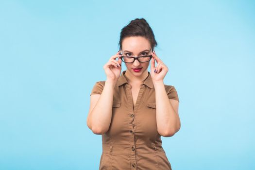 Elegant cheerful brunette in eyeglasses smiling at camera on blue background.