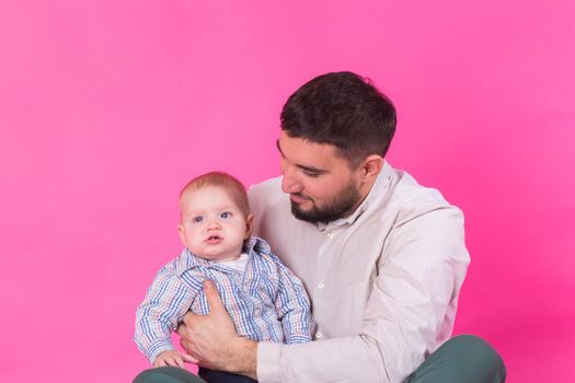 Happy portrait of the father and son on pink background. In studio.