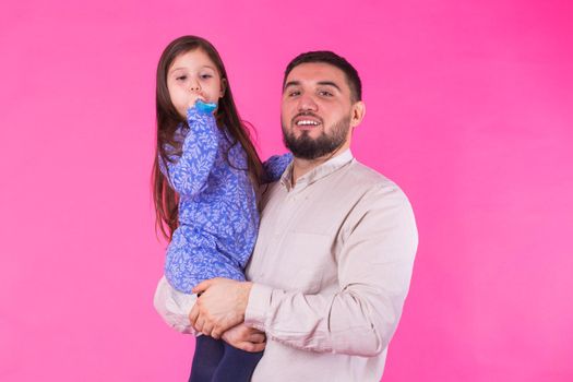 Happy father holding baby daughter in hands over pink background.