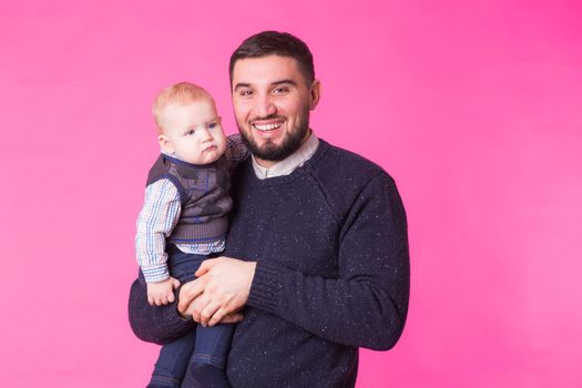 Happy father holding baby son in hands over pink background.