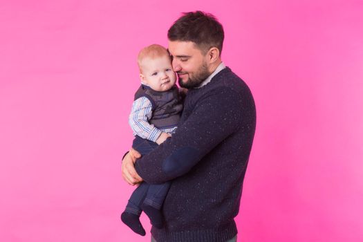 Happy father holding baby son in hands over pink background.