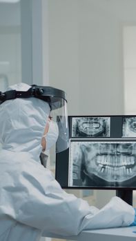 Medical dentistry staff with ppe suits using modern technology while consulting patient with oral care issues. Stomatologist and dental nurse looking at teeth animation model for implant