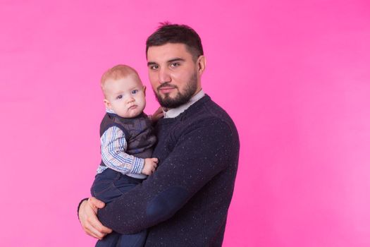 Happy father holding baby son in hands over pink background.