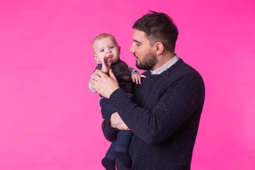 Happy portrait of the father and son on pink background. In studio.