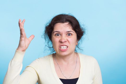 Angry aggressive woman with ferocious expression on blue background.