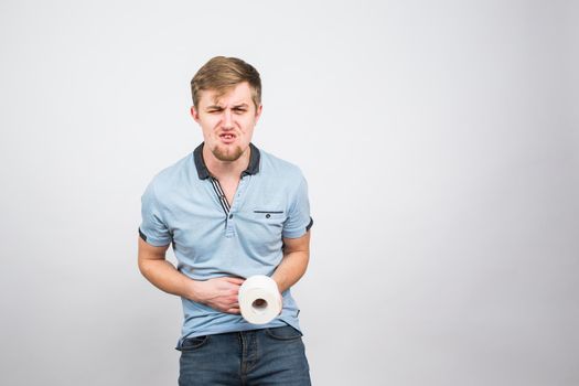 Man with stomach pain and toilet paper roll on white background.