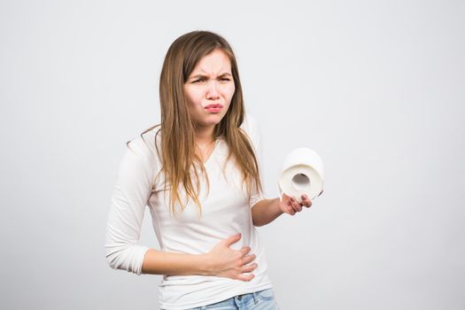 Woman with stomach pain and toilet paper roll on white background.