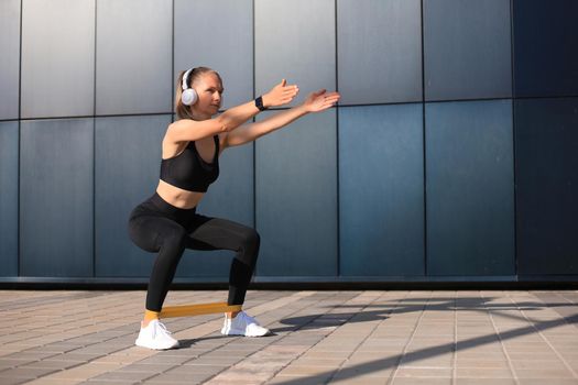 Sporty woman doing squats with fitness gum expander outdoors