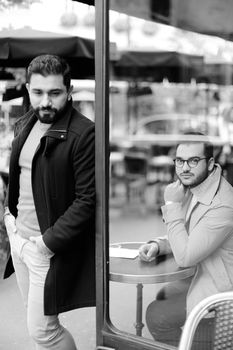 Black and white photo of young stylish guy standing at street cafe outdoors. Concept of life style and male fashion.