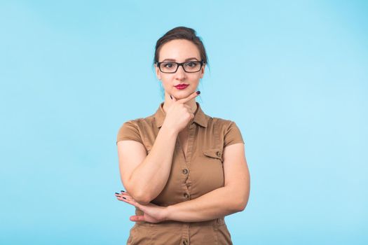 Elegant cheerful brunette in eyeglasses smiling at camera on blue background.