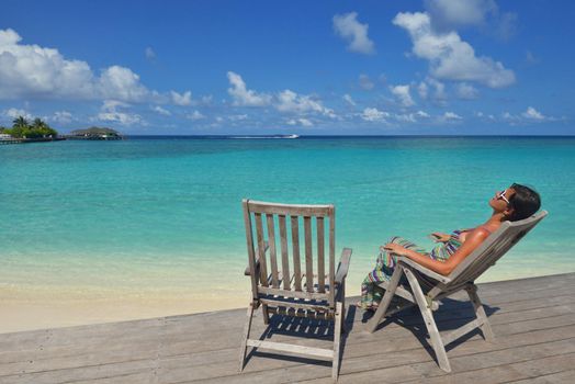 Beautiful young woman in bikini lying on a deckchair with a drink by the sea