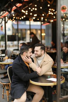 Caucasian smiling gays sitting at street cafe and hugging. Concept of relationship and same sex couple.