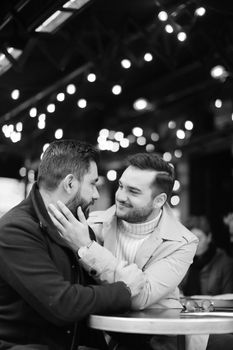 Black and white photo of caucasian happy gays sitting at street cafe and hugging. Concept of relationship and same sex couple.