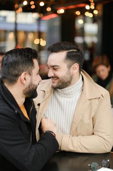 Caucasian gays sitting at street cafe, smiling and hugging. Concept of relationship and same sex couple.