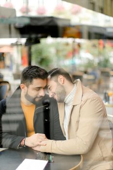 Caucasian gays sitting at street cafe and hugging, reflection in glass. Concept of relationship and same sex couple.