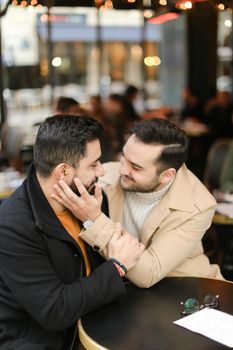 Caucasian gays sitting at street cafe and hugging. Concept of relationship and same sex couple.