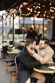 Caucasian happy gays sitting at street cafe and hugging. Concept of relationship and same sex couple.