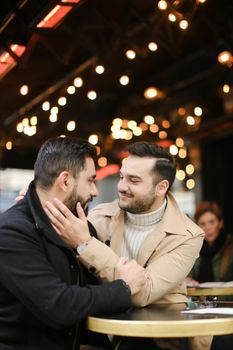 Caucasian gays sitting at street cafe table and hugging. Concept of relationship and same sex couple.