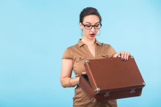 Portrait of excited young woman holding a suitcase isolated over blue background, Travel, holidays and vacation concept