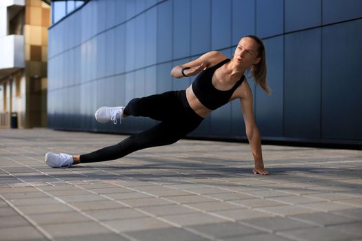 Fitness woman in sportswear doing side plank exercise outdoors