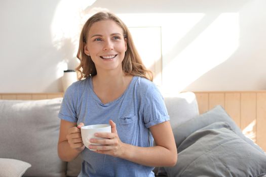 Young woman sitting in armchair and drinking coffee