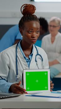 Medical specialist with horizontal green screen on digital tablet in cabinet, analyzing isolated background with senior patient. Doctor holding mockup template and chroma key technology.