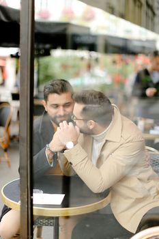 Two young handsome gays talking at street cafe and holding hands. Concept of same sex couple and lgbt.