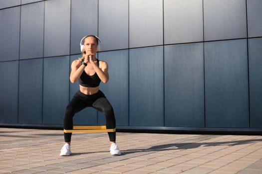 Sporty woman doing squats with fitness gum expander outdoors