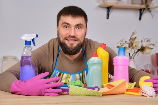Image of a young Caucasian bearded man in the kitchen, he makes little presentation of all his detergents, preparing for big cleaning