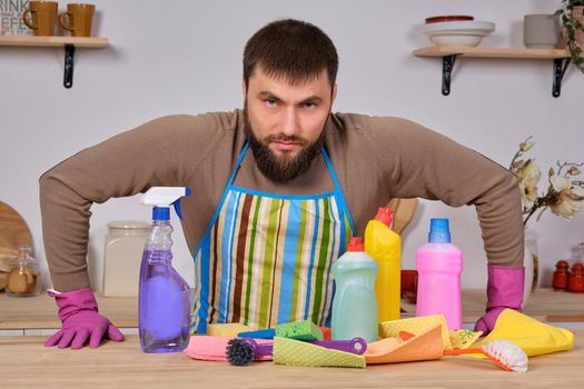 Image of a young Caucasian bearded man in the kitchen, he makes little presentation of all his detergents, preparing for big cleaning