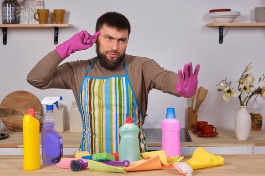Image of a young Caucasian bearded man in the kitchen, he makes little presentation of all his detergents, preparing for big cleaning