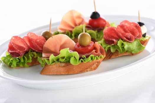 Tender baguette canapes with Leaf lettuce, salami or Parma ham, tomatoes, mozzarella and olive. Delicacy assorted platter for at the party.