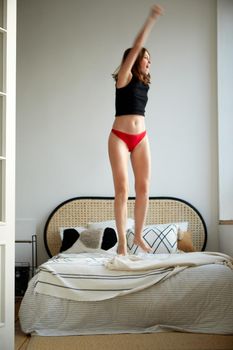 Delighted carefree female in t shirt and panties jumping on soft bed while having fun at home
