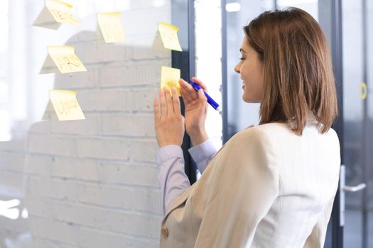 Attractive busness woman post stickers on glass at office and writing on them