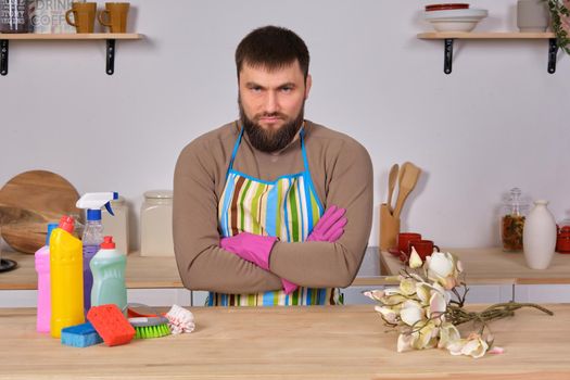 Image of a young Caucasian bearded man in the kitchen, he makes little presentation of all his detergents, preparing for big cleaning. Man caring for flowers