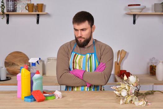 Image of a young Caucasian bearded man in the kitchen, he makes little presentation of all his detergents, preparing for big cleaning. Man caring for flowers