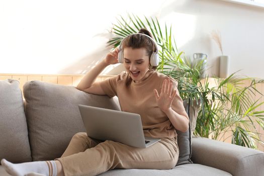 Smiling young woman with headphones and laptop on the sofa