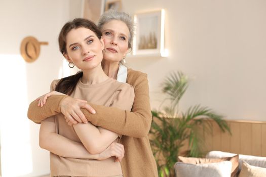 Beautiful mother and daughter. Cheerful young woman is embracing her middle aged mother in living room. Family portrait