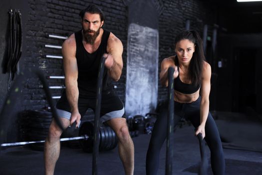 Athletic young couple with battle rope doing exercise in functional training fitness gym