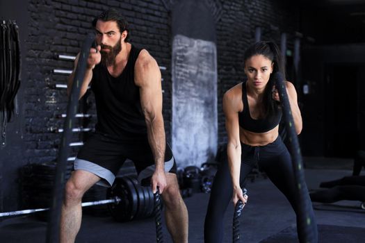 Athletic young couple with battle rope doing exercise in functional training fitness gym