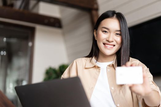 Online shopping. Young woman paying for purchase with credit card, buying on websites on laptop, sitting at home in living room.