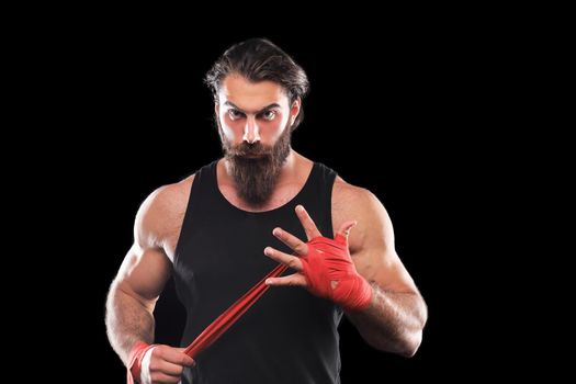 Athlete stands in black clothes and wraps his hands in red textile elastic bandage before training