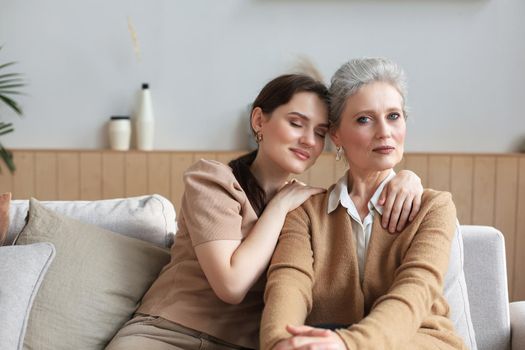 Portrait of old mother and mature daughter hugging at home. Happy senior mom and adult daughter embracing with love on sofa