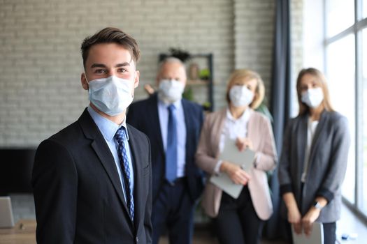 Businessman in medical mask with colleagues in the background in office