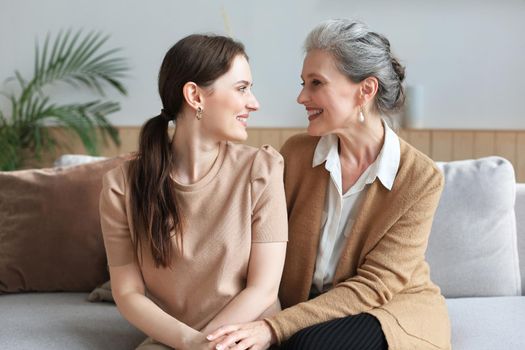 Portrait of old mother and mature daughter hugging at home. Happy senior mom and adult daughter embracing with love on sofa