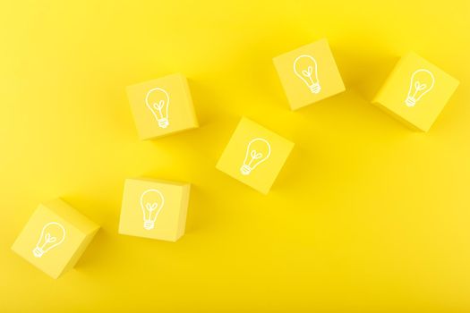 Concept of idea, creativity, start up or brainstorming. Light bulbs drawn on yellow toy cubes on yellow background